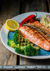 Grilled wild caught salmon on a serving plate with brown rice and grilled broccoli.