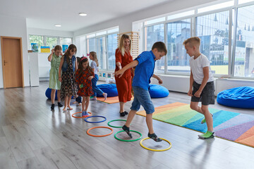 Small nursery school children with female teacher on floor indoors in classroom, doing exercise....