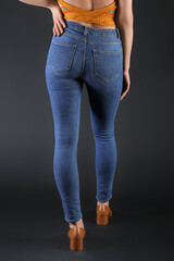 Young woman in skinny jeans on dark background, back view