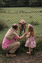 grandfather holds his granddauther and feeds a deer