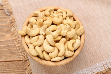 Bowl with tasty cashew nuts on wooden background