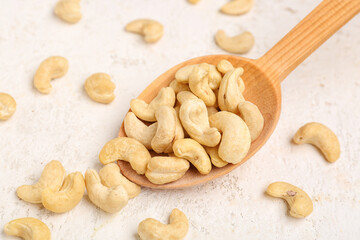 Spoon with tasty cashew nuts on light background