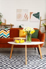 Interior of light living room with cozy brown sofa and narcissus flowers on coffee table