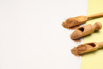Wooden scoops with cinnamon powder on light background