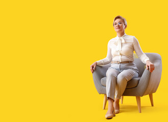 Fototapeta na wymiar Mature psychologist sitting in armchair on yellow background