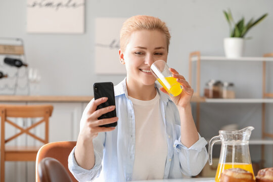 Young woman with mobile phone drinking juice in kitchen