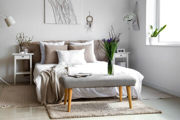 Interior of bright bedroom with beautiful iris flowers on bedside bench