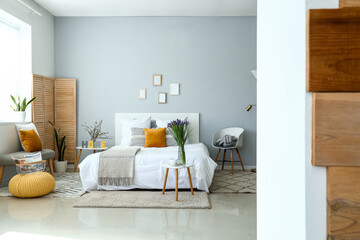 Fototapeta na wymiar Interior of stylish bedroom with blooming iris flowers on bedside table, view through doorway