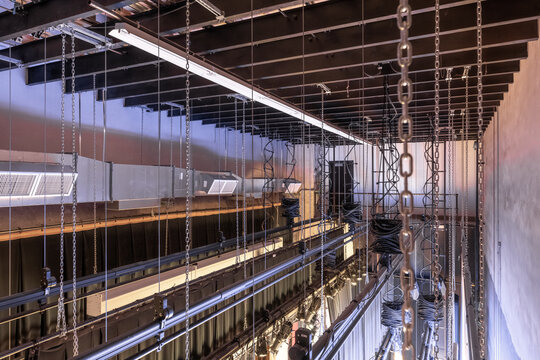 Theater stage rigging with theatrical equipment, lighting, supports, and chains.  Photo taken from an elevated position looking across the rigging.