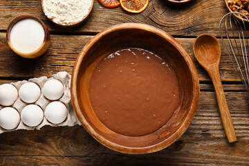 Bowl with dough and ingredients for preparing chocolate brownie on wooden background