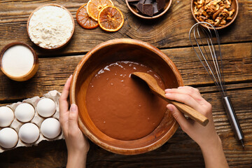 Woman preparing dough for chocolate brownie on wooden background