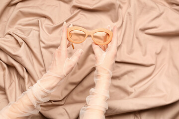 Woman with stylish sunglasses on beige fabric background