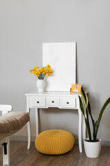 Vase with blooming narcissus flowers, painting and photo frame on dressing table near grey wall