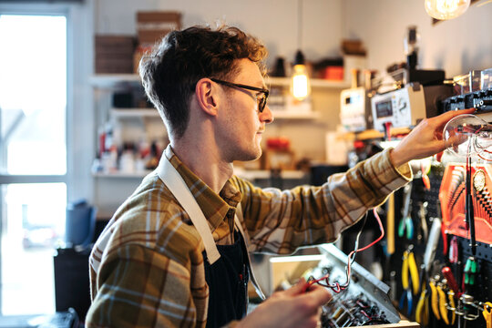 Young repairman working with electronics in own shop