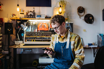 Serious young craftsman using smartphone in workshop