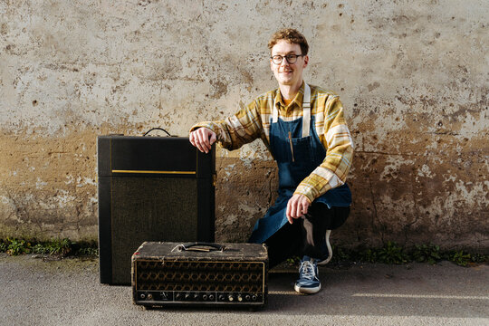 Positive man with guitar amplifiers on pavement