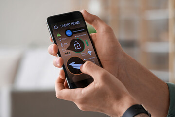 Young man with mobile phone using smart home security system application, closeup