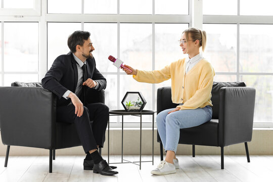 Female journalist with microphone having an interview with man in office