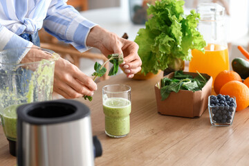 Mature woman adding mint into glass of healthy smoothie in kitchen, closeup