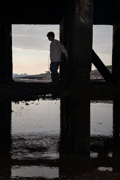 Boy climbs underneath a pier by the coast.