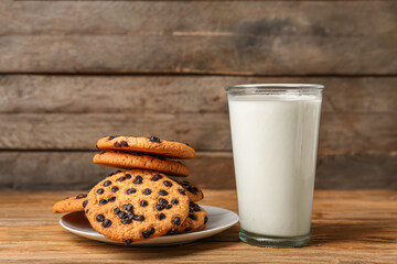 Tasty cookies with chocolate chips and glass of milk on wooden background