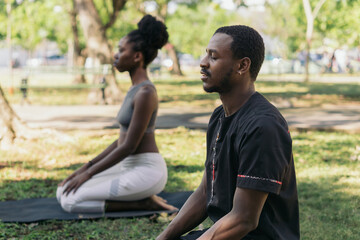 Profile portrait of a couple meditating in the park.
