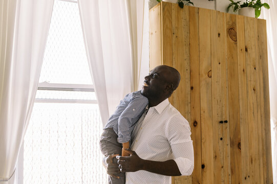 Happy smiling black father holding his son in arms at home 