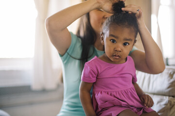 asian mom styling her mixed race daughter's hair in living room 