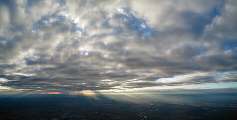 Aerial view from airplane window at high altitude of distant city covered with white puffy cumulus clouds