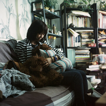 The woman is sitting on the sofa holding a teddy dog