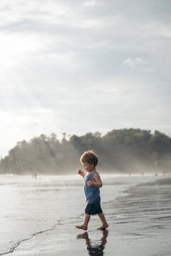 Toddler walks to calm beach at sunset.