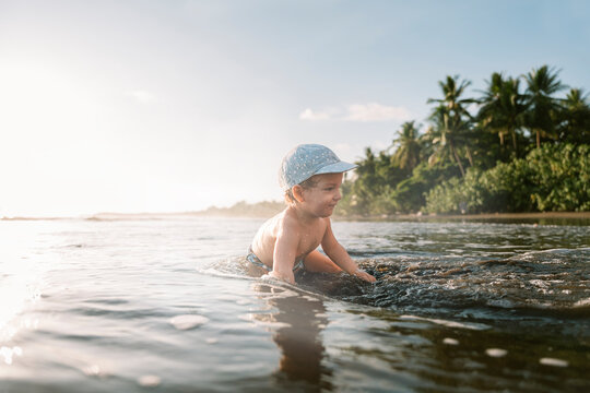Child in hat enjoying by seaside palms.