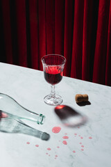 Pouring red wine into glass against red curtained background