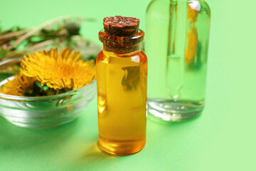 Bottles with cosmetic oil and bowl of dandelion flowers on green background