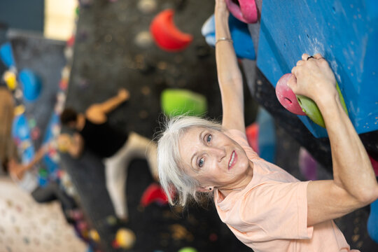 Determined senior woman doing her best at climbing artificial wall