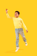 Little African-American boy with paper plane on yellow background. Children's Day celebration