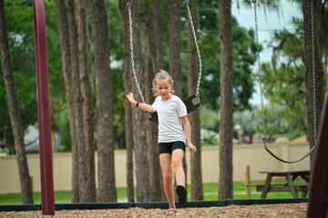 Young pretty excited teenage girl jumping out of the swings on summer vacations sunny day. Danger of accident concept