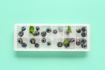 Ice tray with fresh blueberry frozen in ice on blue background