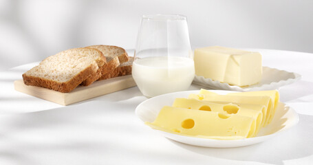 dairy products on a light background. milk cheese bread and butter on a white tablecloth close-up. slices of gouda cheese. piece of butter and a glass of milk with slices of bread in the background.