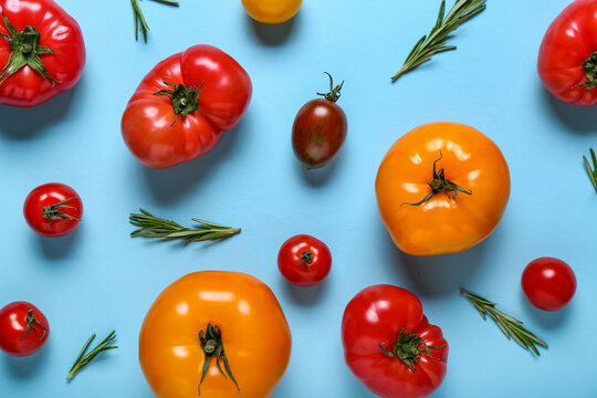 Different fresh tomatoes and rosemary on blue background