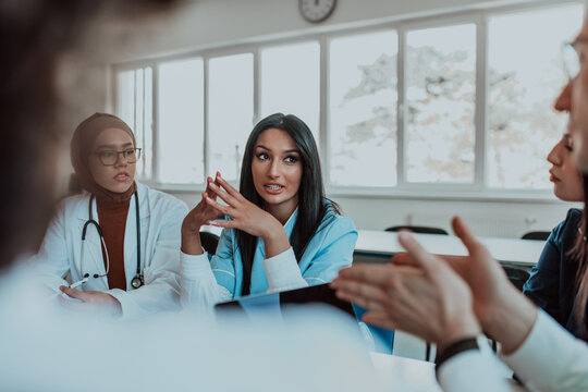 A group of multiethnic medical professionals including doctors, surgeons, and nurses are gathered in a hospital setting discussing patient care and using modern technology to address challenges in