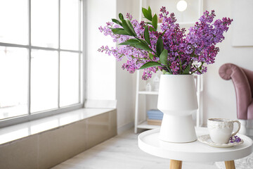 Vase with blooming lilac flowers and cup of tea on coffee table in interior of living room