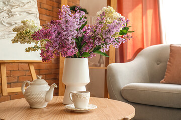 Vase with blooming lilac flowers, teapot and cup on coffee table in living room
