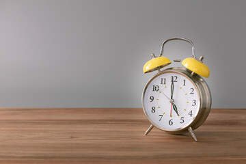 Retro silver alarm clock. 5:00.  am,  pm. Neutral background. Brown wood surface. Horizontal  photography with empty space for text or image.