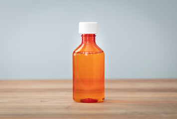 Bottle with liquid medicine. Transparent orange vial with lid on neutral background. Stop your cold today. Copy space for text or image.
