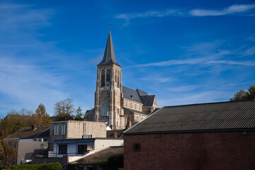 Typical belgian catholic church, a medieval one with its old steeple clocktower, in the limburg countryside, near liege, in Belgium, during a sunny afternoon.