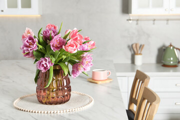 Beautiful bouquet of colorful tulip flowers on white marble table in kitchen, space for text