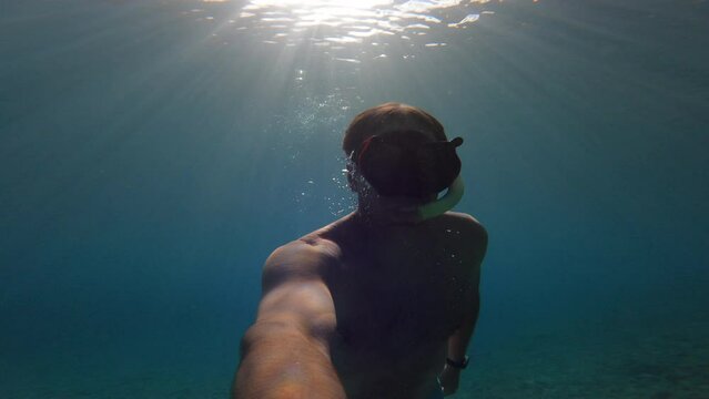 UNDERWATER: Young guy is snorkelling in beautiful clear blue water of Adriatic Sea. He is swimming with fins and watching amazing and peaceful environment under seawater surface through diving mask.