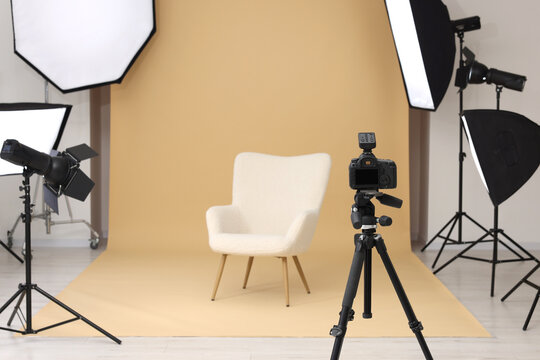 Camera on tripod, armchair and professional lighting equipment in modern photo studio, space for text