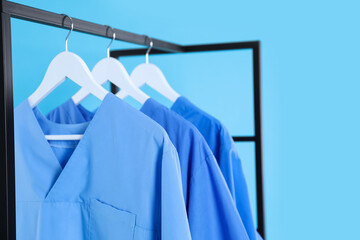 Medical uniforms on metal rack against light blue background, closeup
